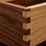 An extreme close-up of the corner of a wooden drawer, clearly showing the interlocking teeth of a dovetail joint.